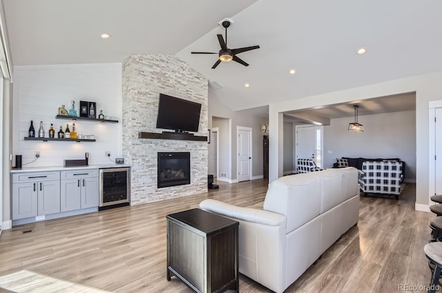 living room featuring beverage cooler, lofted ceiling, indoor bar, a fireplace, and light hardwood / wood-style flooring