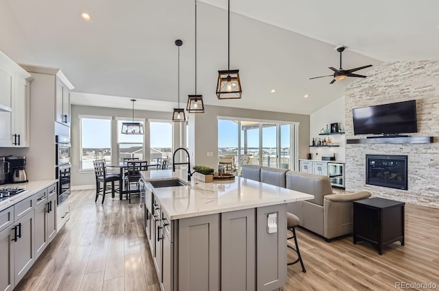 kitchen featuring a kitchen bar, an island with sink, decorative light fixtures, lofted ceiling, and light stone counters