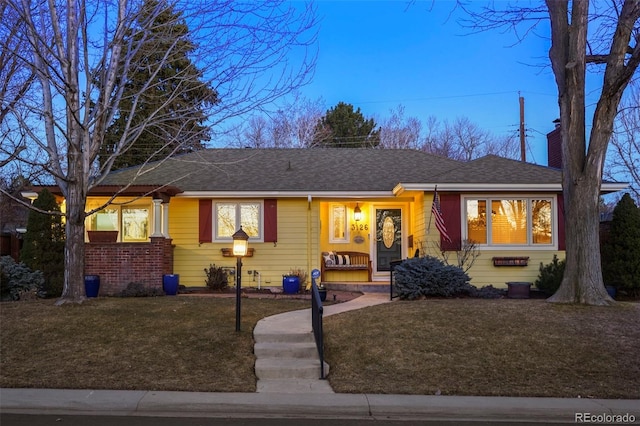 view of front facade featuring brick siding, a chimney, a front yard, and a shingled roof