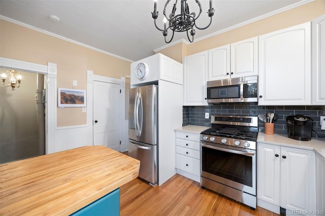 kitchen featuring white cabinets, light wood-style flooring, ornamental molding, stainless steel appliances, and a notable chandelier