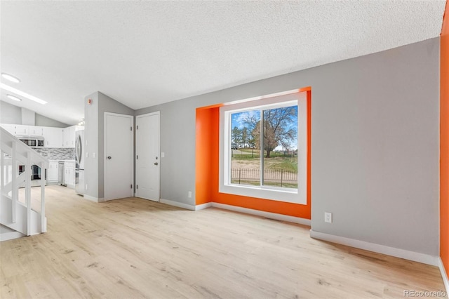unfurnished living room featuring baseboards, vaulted ceiling, light wood finished floors, and a textured ceiling