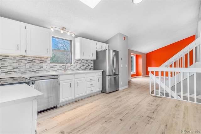 kitchen featuring appliances with stainless steel finishes, a sink, light wood-style flooring, white cabinetry, and tasteful backsplash