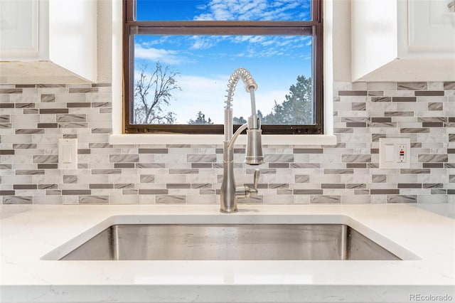 room details featuring a sink, light countertops, tasteful backsplash, and white cabinets