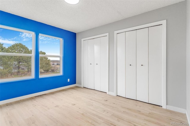 unfurnished bedroom featuring a textured ceiling, two closets, baseboards, wood finished floors, and visible vents
