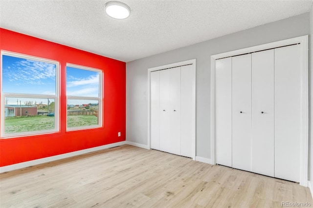 unfurnished bedroom featuring baseboards, a textured ceiling, multiple closets, and wood finished floors