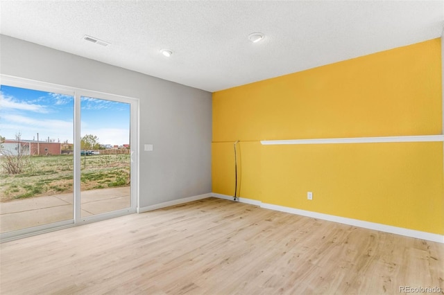 spare room featuring a textured ceiling, baseboards, visible vents, and wood finished floors