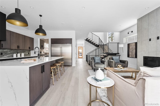 kitchen with a kitchen breakfast bar, pendant lighting, light hardwood / wood-style flooring, built in refrigerator, and dark brown cabinets