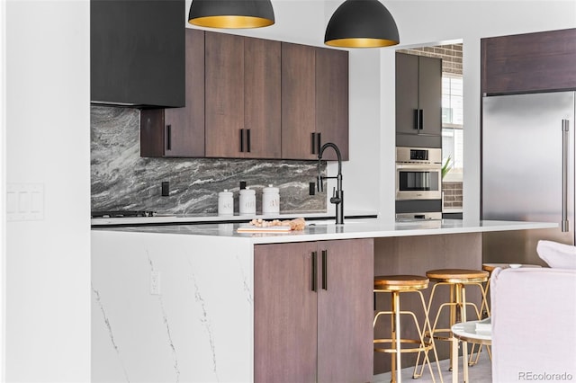 kitchen featuring dark brown cabinets, backsplash, stainless steel appliances, and a kitchen breakfast bar