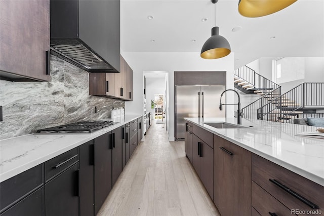 kitchen featuring premium range hood, decorative light fixtures, sink, tasteful backsplash, and light hardwood / wood-style floors