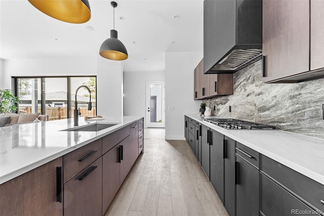 kitchen featuring wall chimney exhaust hood, hanging light fixtures, light wood-type flooring, sink, and tasteful backsplash