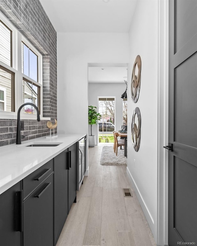 kitchen with wine cooler, light wood-type flooring, gray cabinetry, sink, and tasteful backsplash