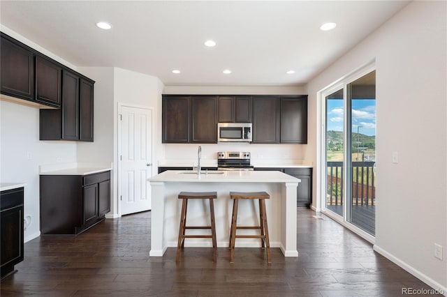 kitchen featuring stainless steel appliances, dark hardwood / wood-style flooring, sink, a breakfast bar area, and a kitchen island with sink