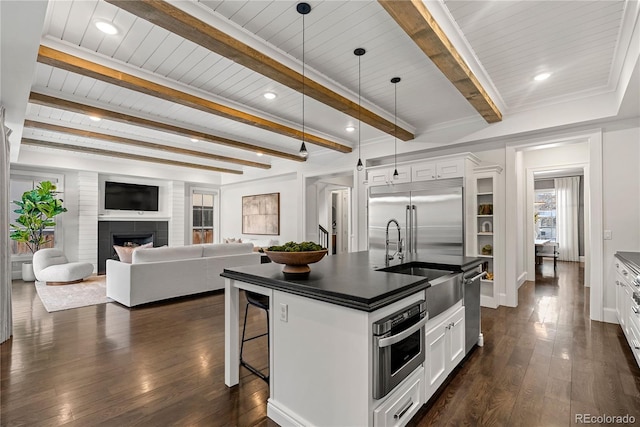 kitchen with appliances with stainless steel finishes, dark countertops, white cabinets, and a center island with sink