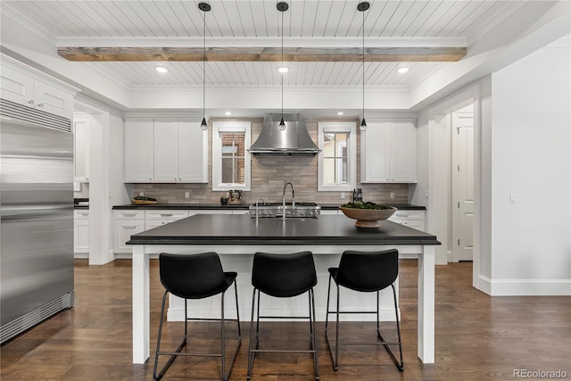 kitchen with dark countertops, wall chimney range hood, pendant lighting, and stainless steel built in refrigerator