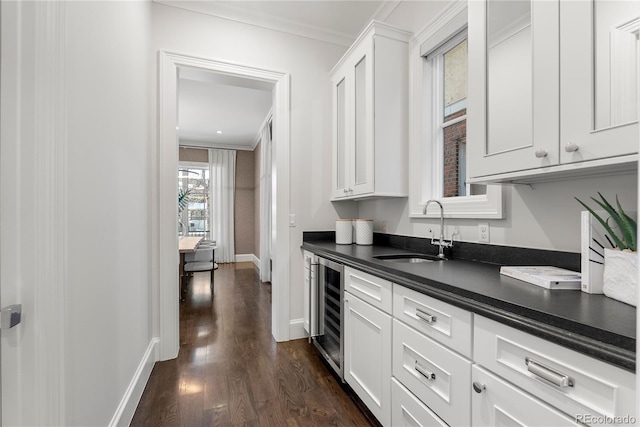 kitchen with beverage cooler, dark countertops, a sink, and white cabinetry