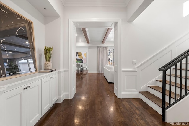 hall with beam ceiling, a decorative wall, dark wood-type flooring, wainscoting, and stairs