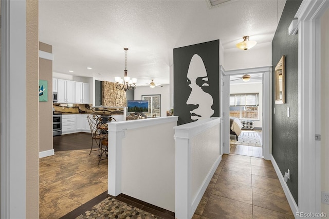 interior space with white cabinets, range, a textured wall, stainless steel microwave, and ceiling fan with notable chandelier