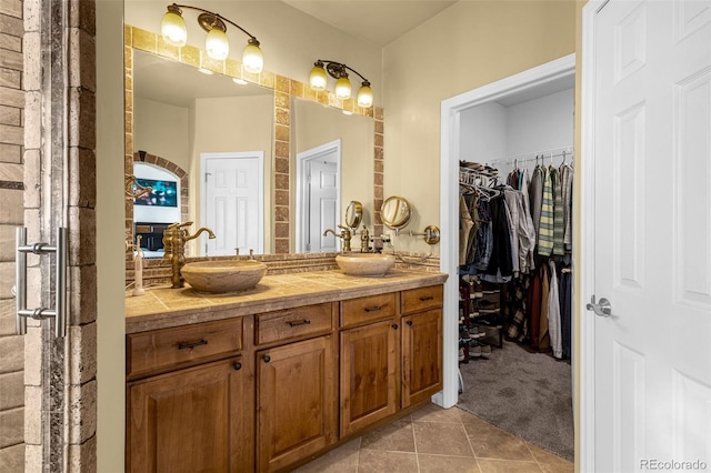 full bath with double vanity, tile patterned flooring, a sink, and a walk in closet