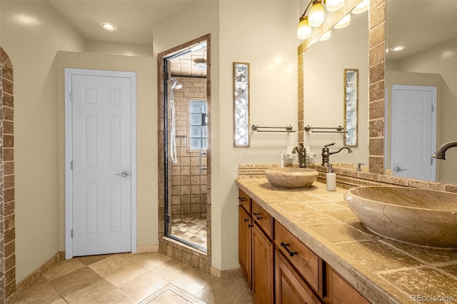 full bathroom featuring baseboards, double vanity, a sink, and a shower stall