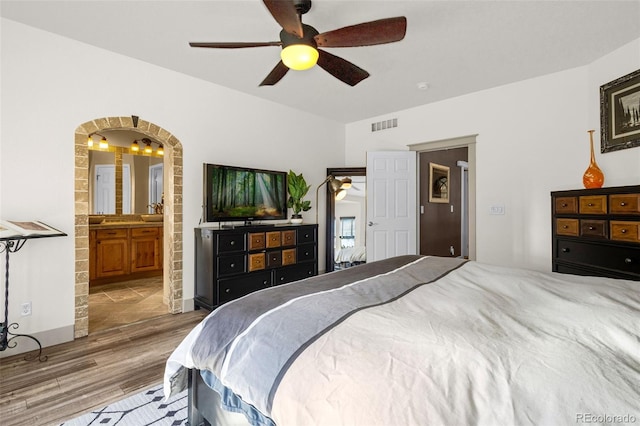 bedroom with visible vents, arched walkways, a ceiling fan, connected bathroom, and wood finished floors