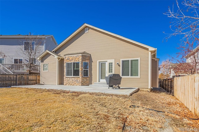 back of house with entry steps, a patio, a fenced backyard, stone siding, and a lawn