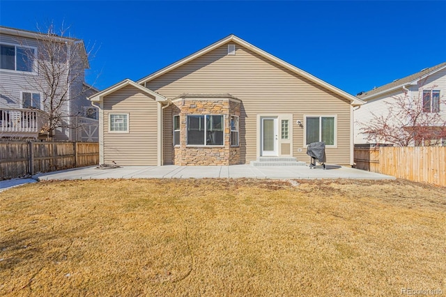 back of property with stone siding, a fenced backyard, a yard, and a patio