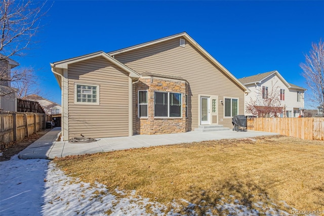 rear view of property with entry steps, a patio, fence, stone siding, and a yard