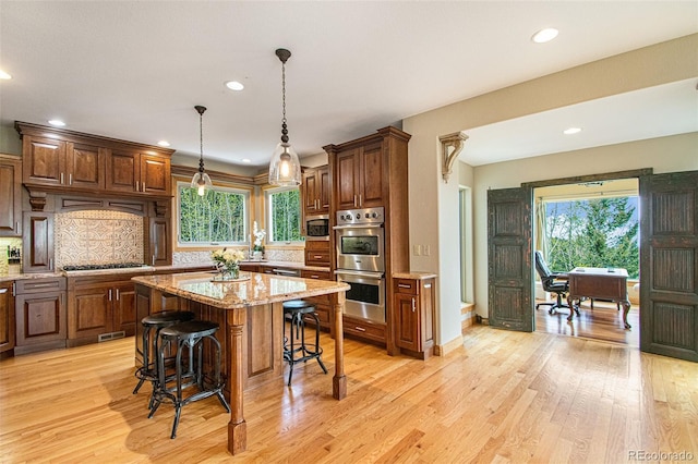 kitchen featuring appliances with stainless steel finishes, a center island, light stone counters, light hardwood / wood-style floors, and decorative backsplash