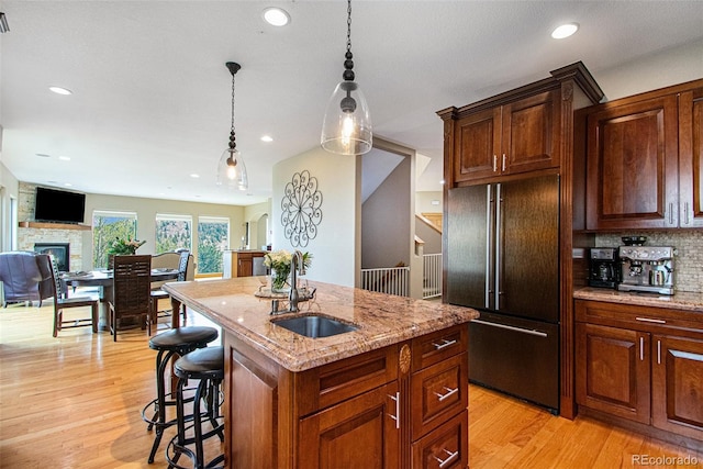 kitchen with sink, high quality fridge, a fireplace, light stone countertops, and a kitchen island with sink