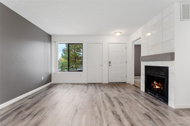 unfurnished living room with light hardwood / wood-style floors, a textured ceiling, and a tile fireplace