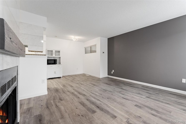 unfurnished living room with a textured ceiling, a tiled fireplace, and light wood-type flooring