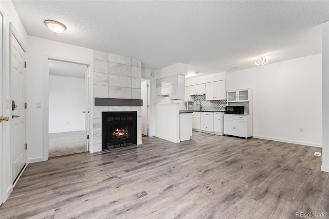 unfurnished living room featuring light hardwood / wood-style floors, a textured ceiling, and a tiled fireplace