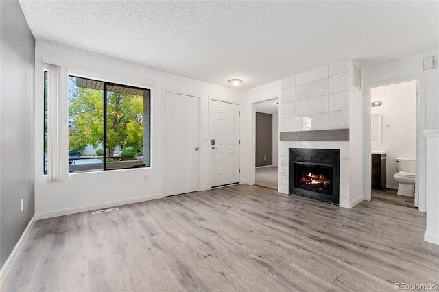 unfurnished living room featuring a fireplace, a textured ceiling, and light hardwood / wood-style floors