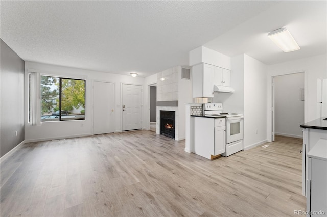 kitchen featuring a textured ceiling, white cabinetry, white range with electric stovetop, a fireplace, and light hardwood / wood-style floors