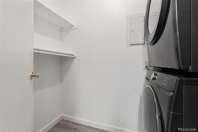 washroom featuring electric panel, stacked washer / dryer, and hardwood / wood-style floors