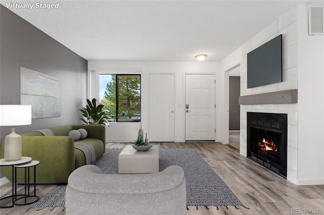 living room with a textured ceiling, light hardwood / wood-style floors, and a tiled fireplace