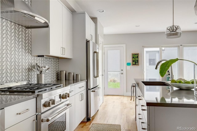 kitchen with tasteful backsplash, decorative light fixtures, wall chimney range hood, stainless steel appliances, and white cabinets