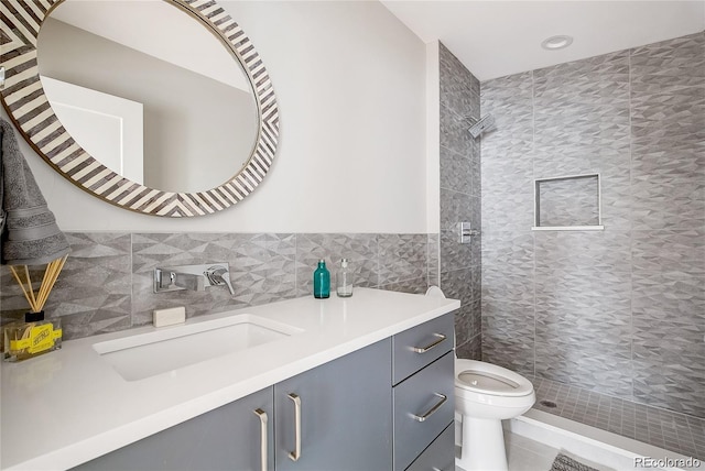 bathroom with vanity, toilet, tile walls, and a tile shower