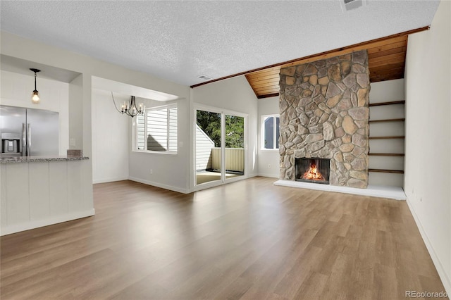 unfurnished living room with lofted ceiling, hardwood / wood-style floors, a notable chandelier, a textured ceiling, and a fireplace