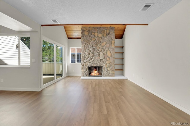 unfurnished living room featuring lofted ceiling, a textured ceiling, a fireplace, and light hardwood / wood-style flooring