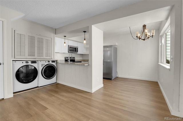 clothes washing area with an inviting chandelier, washing machine and clothes dryer, light hardwood / wood-style flooring, and a textured ceiling