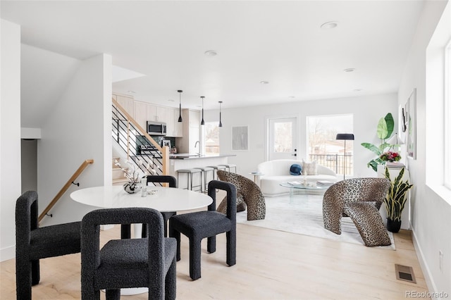 dining room featuring baseboards, visible vents, stairway, and light wood finished floors