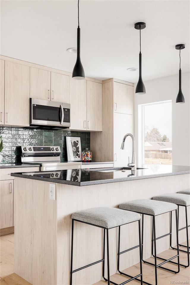 kitchen with stainless steel appliances, decorative light fixtures, and light brown cabinetry