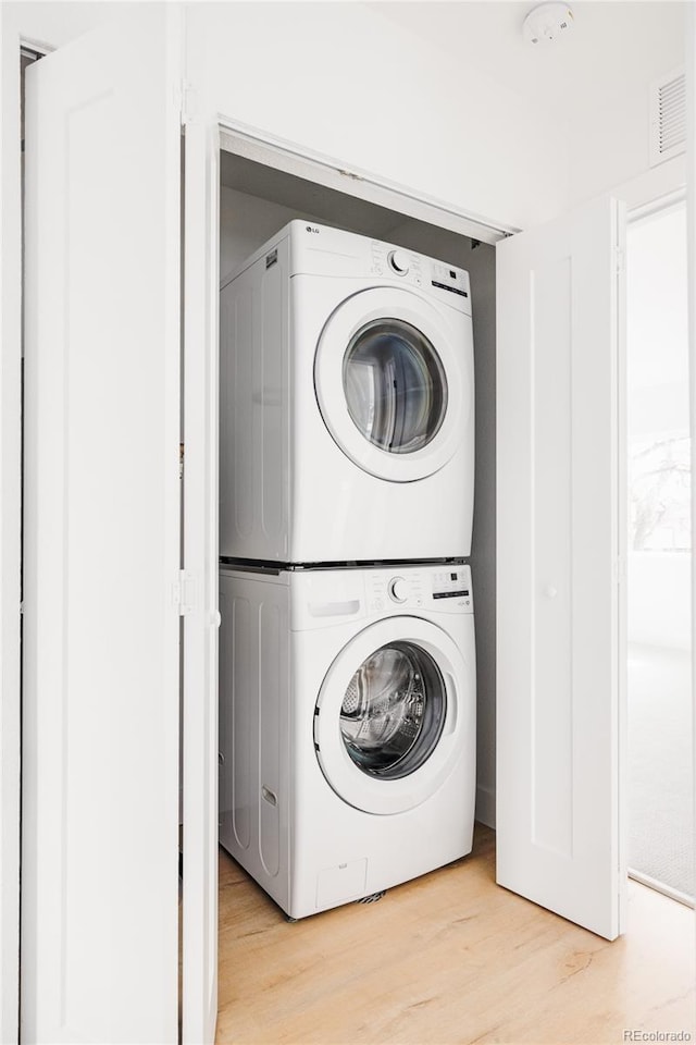 washroom featuring laundry area, light wood-style flooring, visible vents, and stacked washer / dryer