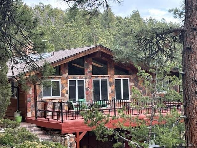 rear view of property with a deck, stone siding, and a view of trees