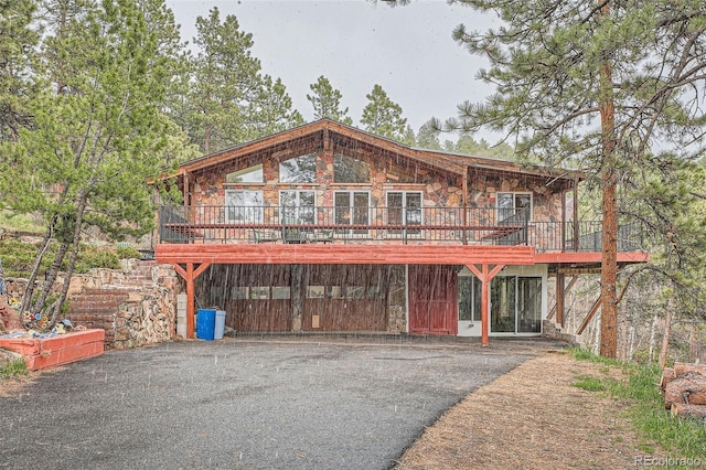 view of front of property with stone siding, a wooden deck, and aphalt driveway
