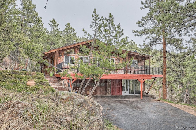 rustic home with stone siding, stairway, a wooden deck, and aphalt driveway
