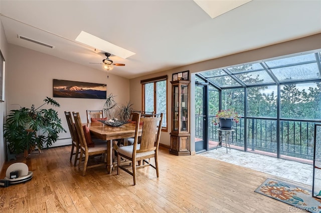 dining space with visible vents, ceiling fan, a sunroom, light wood-type flooring, and vaulted ceiling with skylight