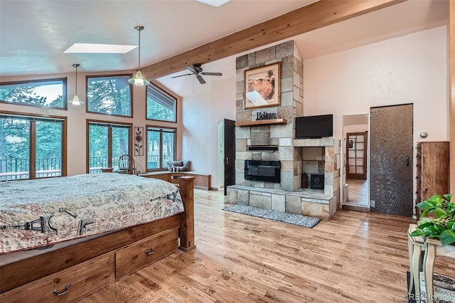 bedroom featuring a stone fireplace, multiple windows, wood finished floors, beamed ceiling, and a skylight