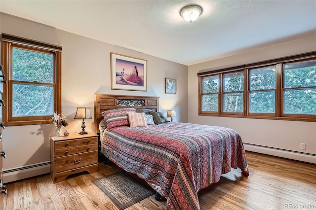 bedroom with multiple windows, wood finished floors, and baseboard heating